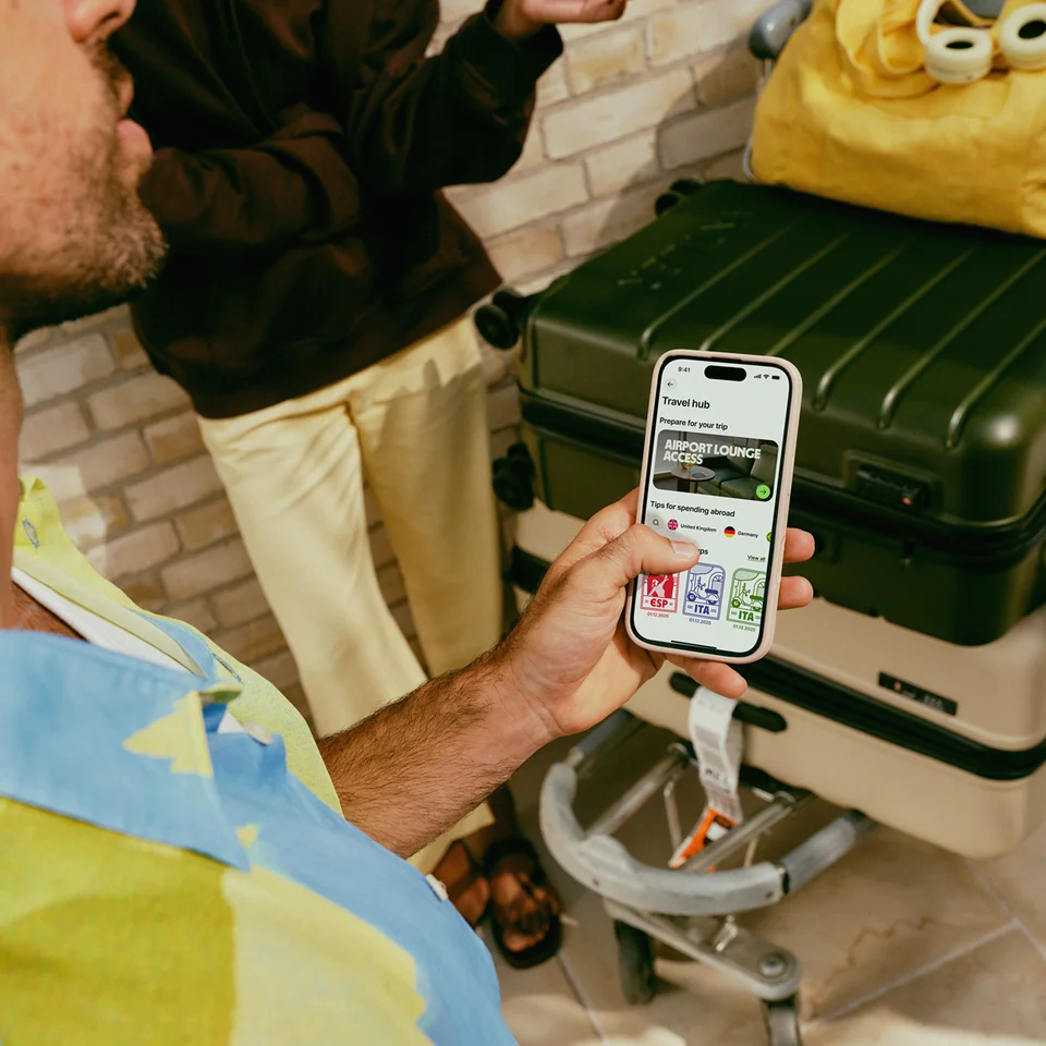A man holding a smartphone with suitcases in the background. His airport lounge pass is loaded on his phone.