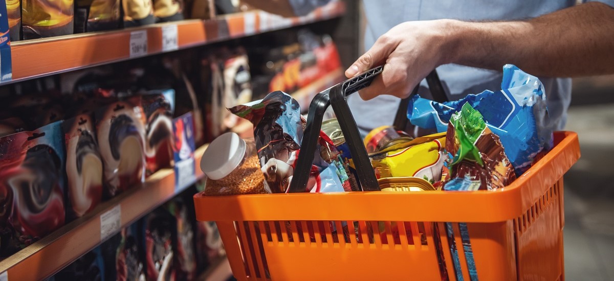 Close up of a male hand holding an orange shopping basket in a supermarket