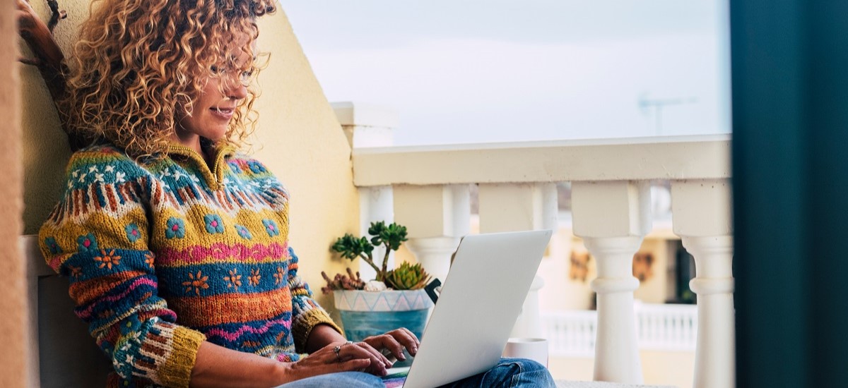 Woman with curly hair working from home on laptop on terrace in Portugal