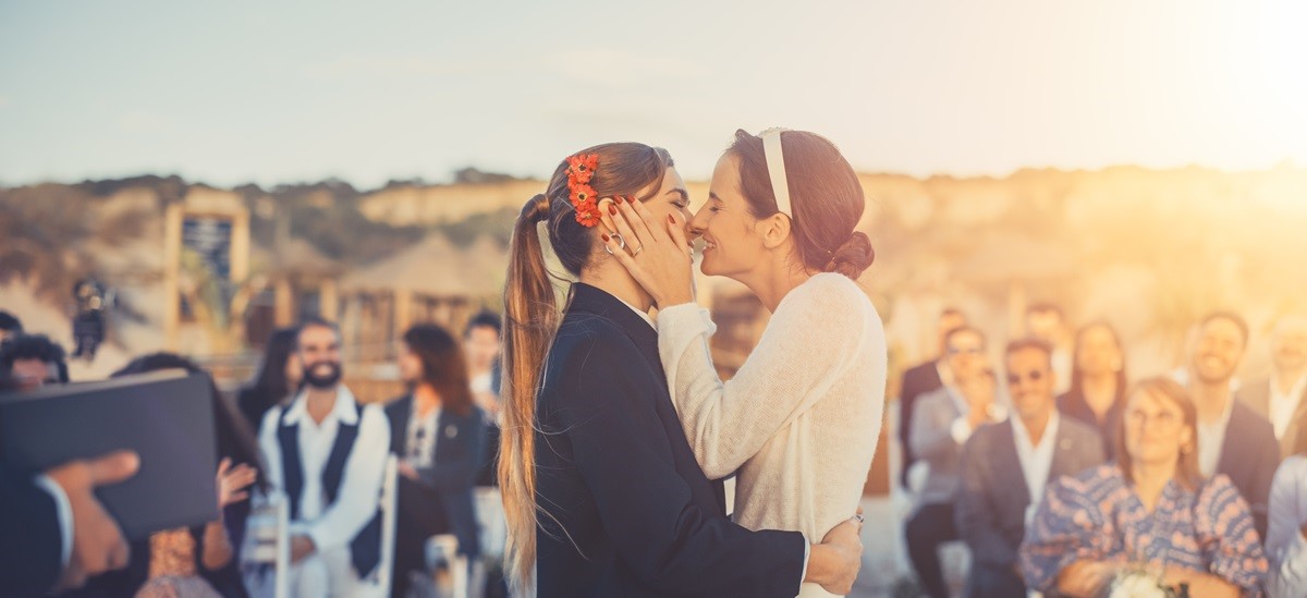 two women in a same sex couple kissing during wedding ceremony