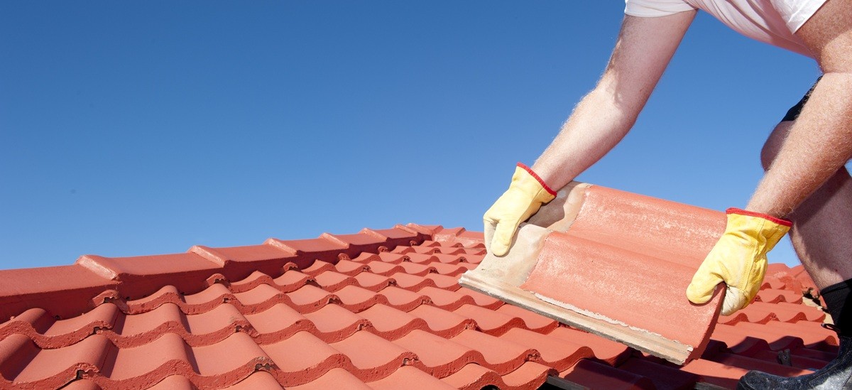 close up of builder placing tiles with a blue sky in background