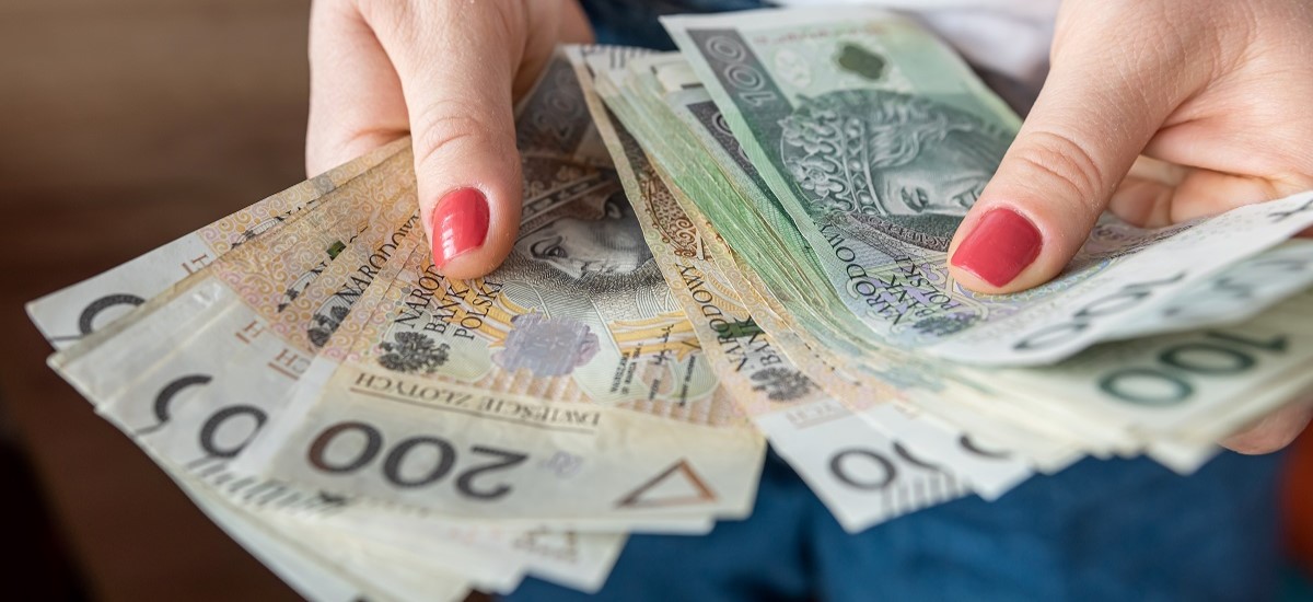 Close-up of a white hand with red nail polish fanning out lots of Polish złoty banknotes