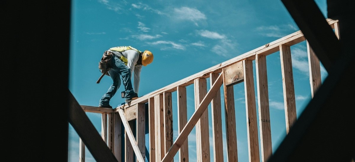 Construction workder standing on a wooden frame of a house with a back drop of clear blue sky