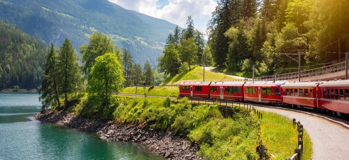 Red train moving along lake in beautiful mountain landscape in Switzerland