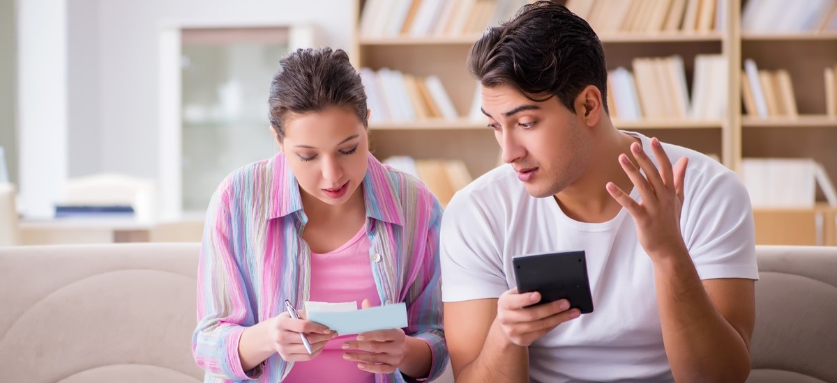 concerned looking couple going over notes together on a sofa, one hold passport