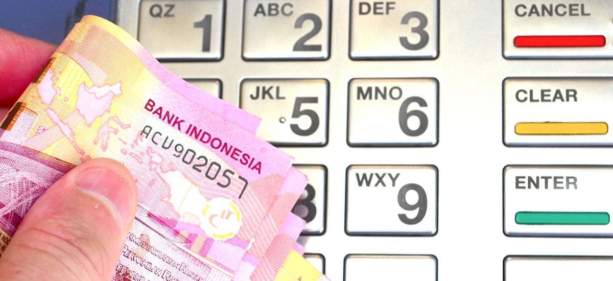 Close of a hand holding Indonesian rupiah notes in front of an ATM pinpad