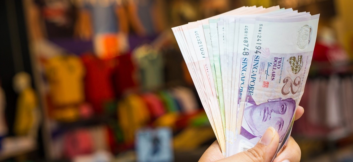 close up of hand holding a fanned out wad of Singapore dollars against a blurred background