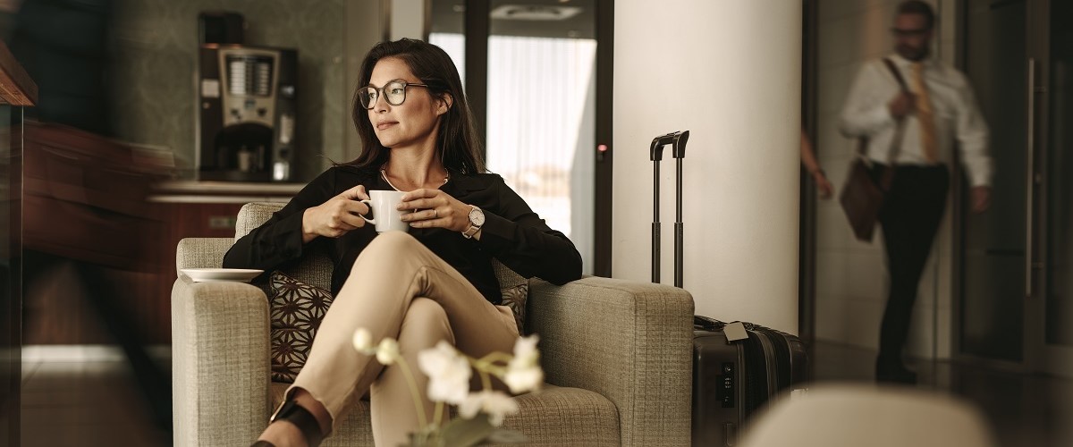 Brunette woman with glasses in an airport lounge holding a cup of coffee