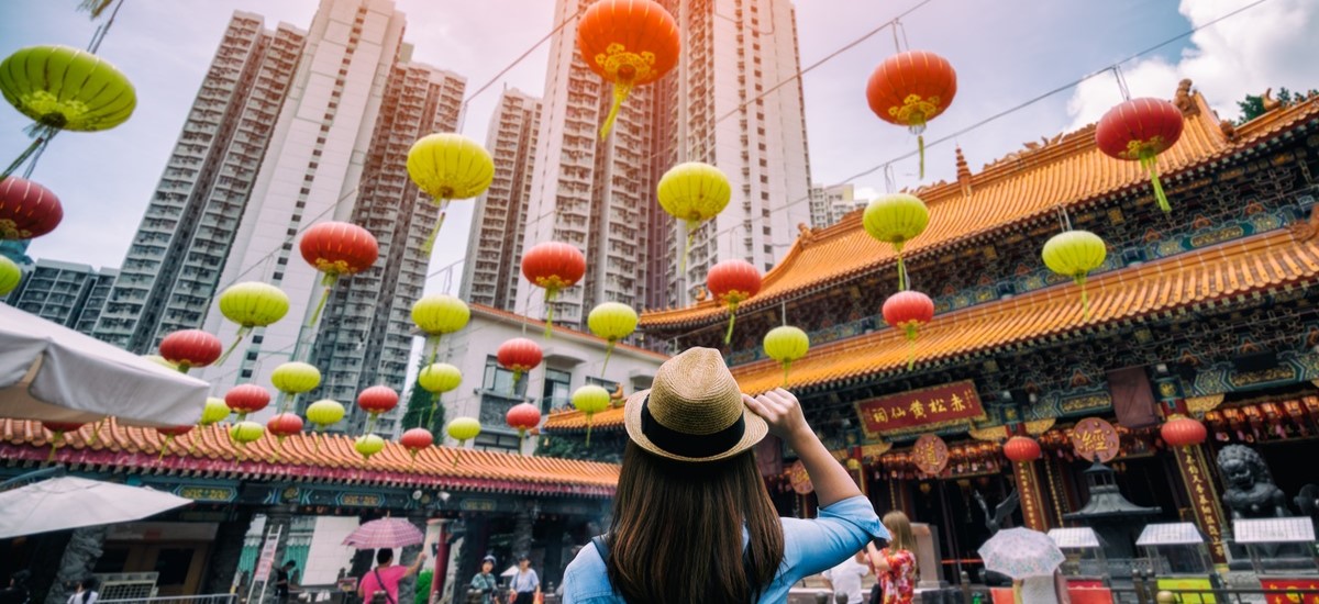 Woman in Wong Tai Sin temple with skyscrapers in distance, Hong Kong