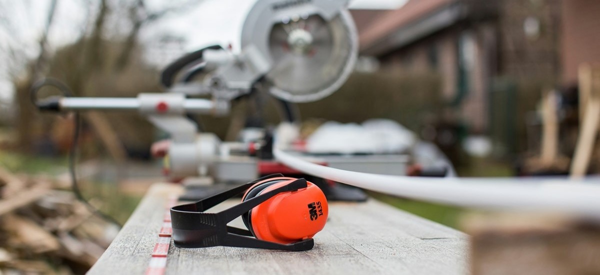 Close up of ear defenders and architectural plans and tools with a house in the background out of focus