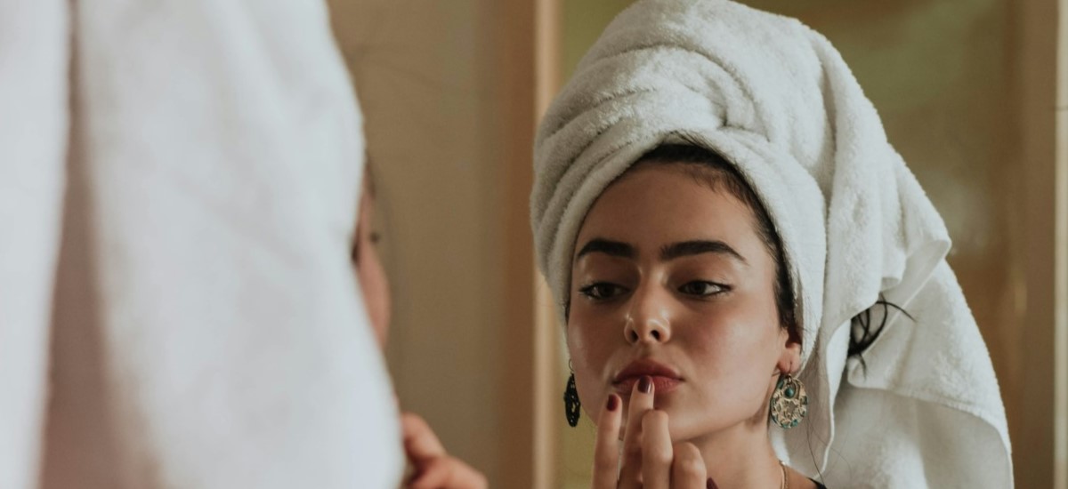 Woman with hair in towel, applying lip tint in mirror