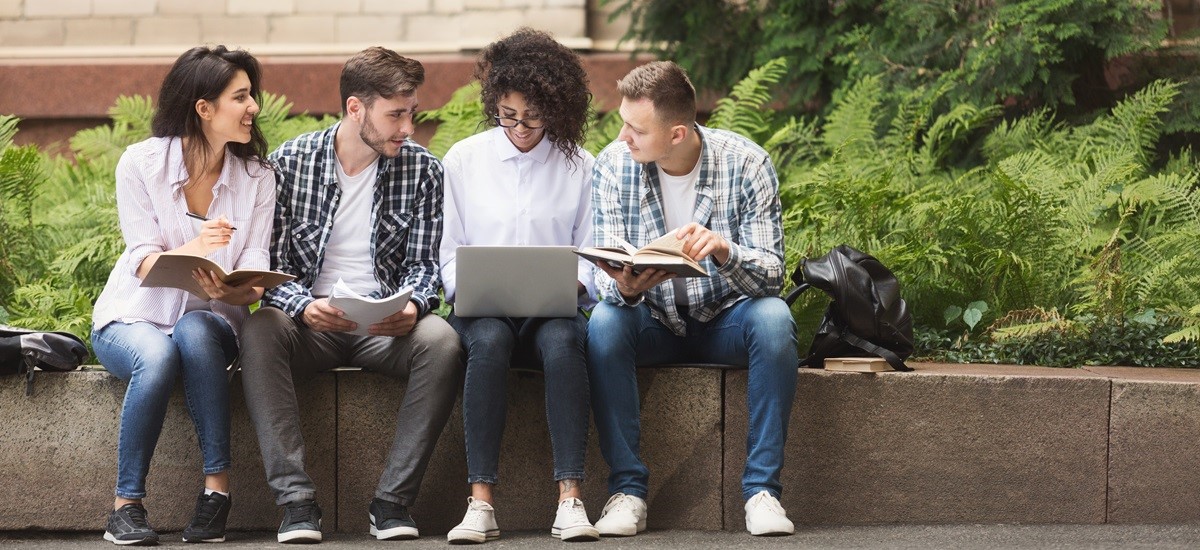 Group of smiling students sitting outside on a wall with a laptop