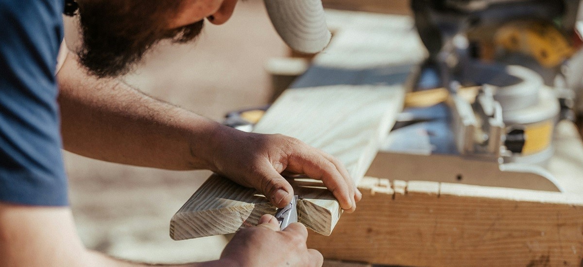 Construction worker leaning over a work bench working on a wooden door frame with a tool