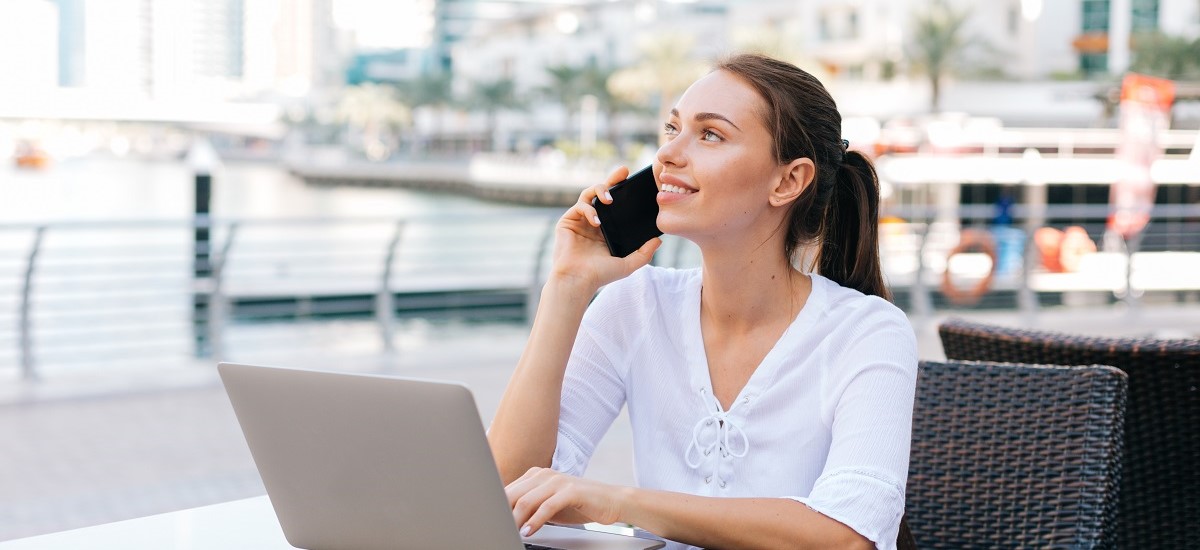 White non-resident woman in Dubai on the phone with a laptop in front of her