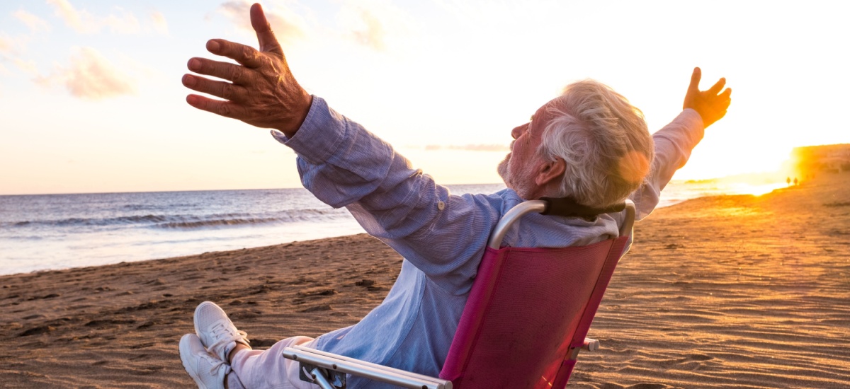 older-man-sitting-on-beach-spreading-arms