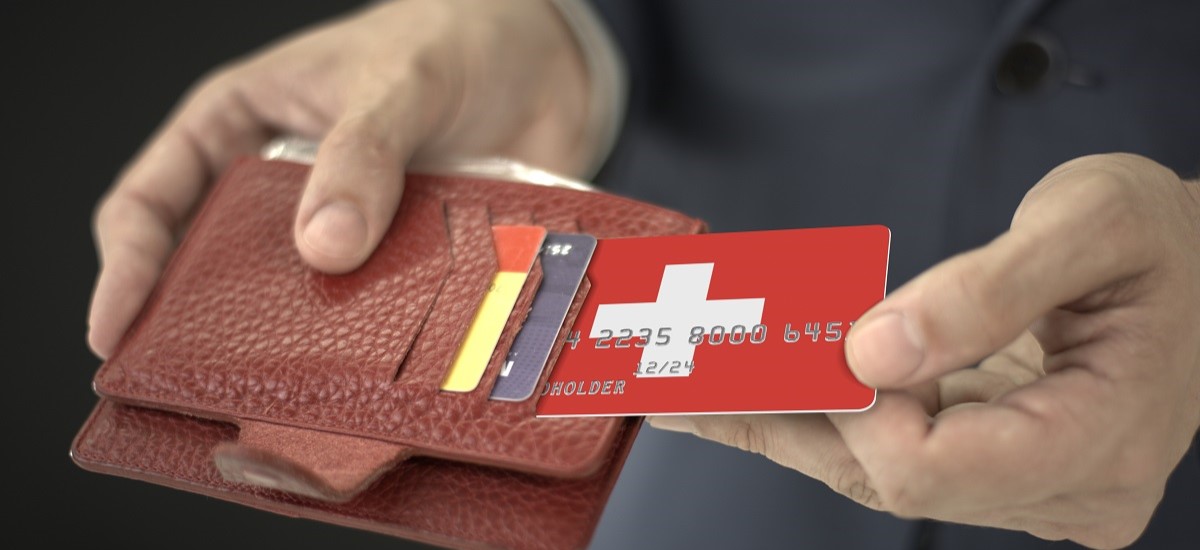 Close up of a bank card with a swiss flag design being taken out of a brown wallet