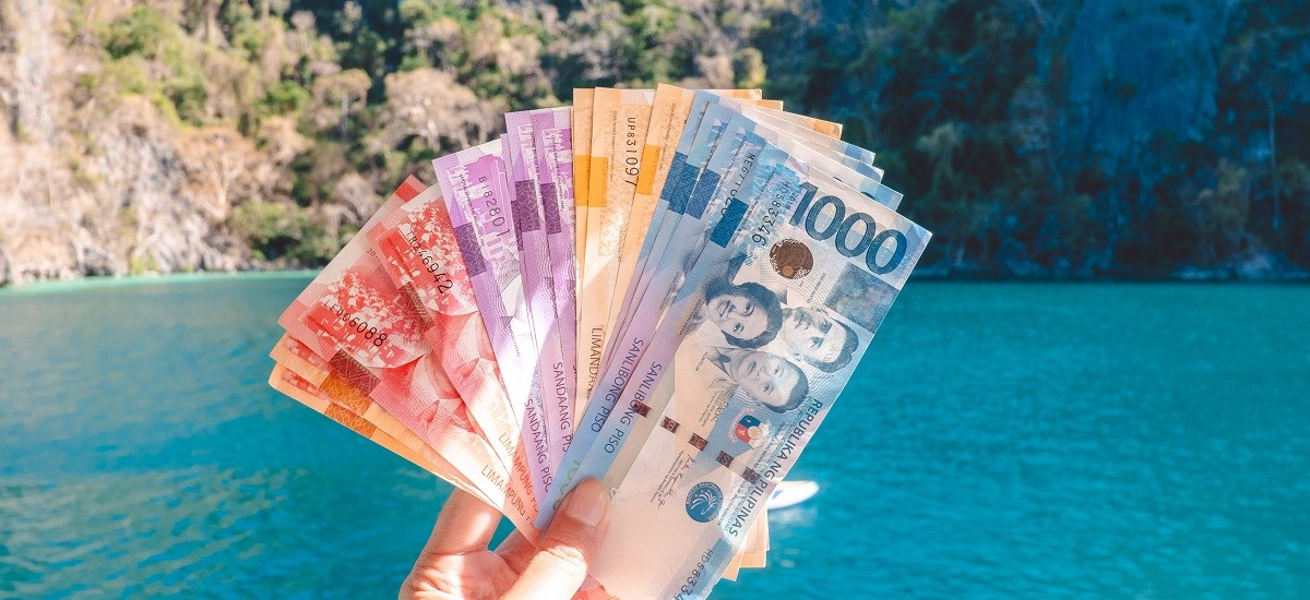 Close-up of hand holding wad of Filipino Pesos in front of Coron El Nido