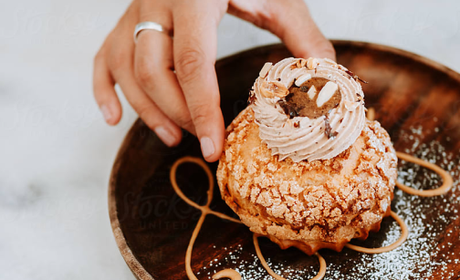 A hand touching a Choux Pastry dessert.