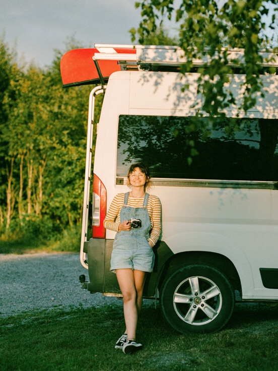 A young woman smiling and leaning against a camper van 