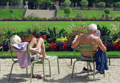 Two people sitting in Jardin du Luxembourg chairs on a sunny day.