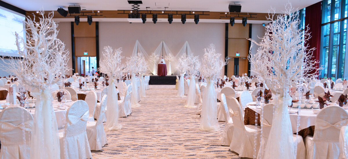 White themed wedding room with flower decoration with Chinese banquet setting in a large hotel ballroom