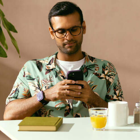 Mężczyzna siedzi przy stole w kawiarni, sprawdzając swoje konto Wise za pomocą aplikacji na smartfony.