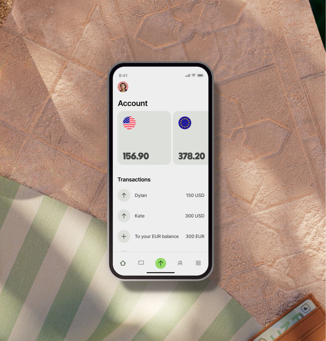 A phone displaying the Wise app sits on a table. The app shows a USD balance and EUR balance, and transactions sending money from the account.